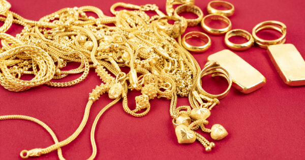 Many gold necklaces and gold bars on red velvet cloth background.